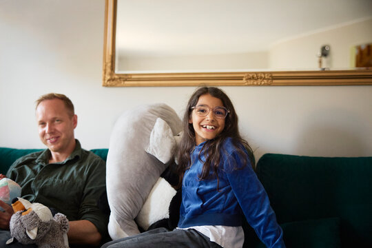 Portrait of smiling girl wearing eyeglasses playing with toy near father on sofa at home