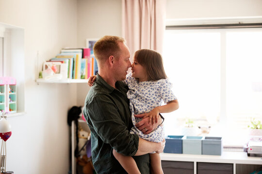 Father rubbing nose with daughter while spending leisure time in bedroom at home