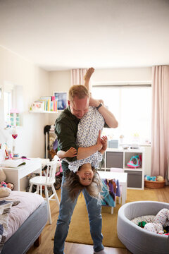 Father carrying daughter upside down while spending leisure time in bedroom at home