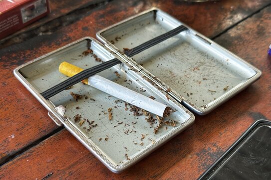 Open Vintage Metal Cigarette Case with Hand-Rolled Cigarette on Wooden Table