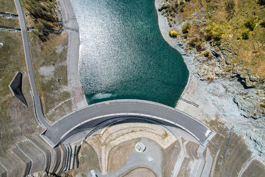 Aerial view of the curved Beauregard Dam wall and turquoise reservoir water surrounded by rocky mountain slopes Valgrisenche, Aosta Valley, Italy.