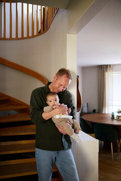 Father embracing baby boy while standing near steps in home