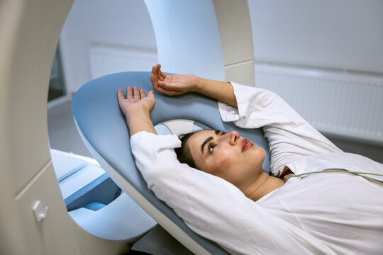Woman lying down with arms raised on sliding table during medical test at clinic
