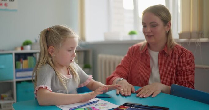 Young girl and supportive teacher practice hands-on learning at a classroom table with colorful materials and educational tools in a bright school setting