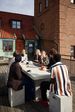 Group of diverse business professionals discussing while sitting around table on office terrace