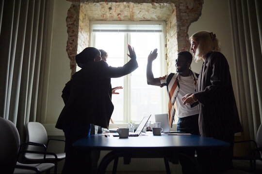 Group of happy business professionals giving high-five in office meeting room