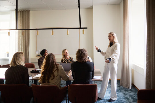 Full length of female manager communicating with coworkers sitting in board room