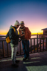 Fototapeta premium Two travelers looking at a smartphone during sunset on a mountain balcony in Chakrata, Uttarakhand, India