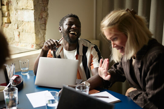 Happy male employee laughing while sitting next to female colleague at office