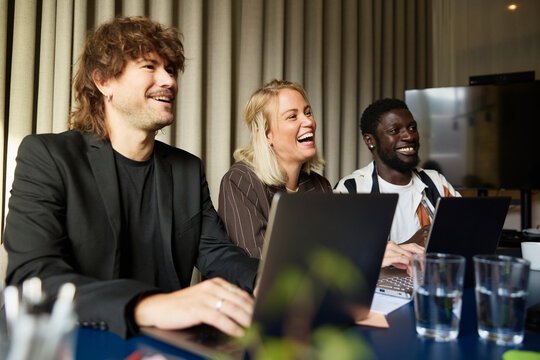 Happy male and female entrepreneurs laughing in business meeting