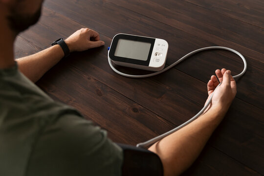 Over the shoulder view of man checking his blood pressure with gauge kept on table in home
