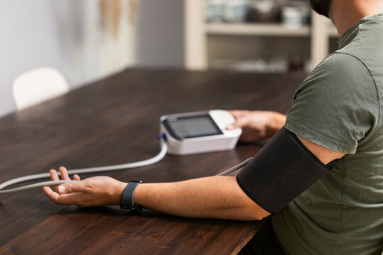 Blood pressure cuff wrapped around arm of man sitting at home