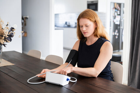 Woman checking her blood pressure on gauge while sitting at table in home