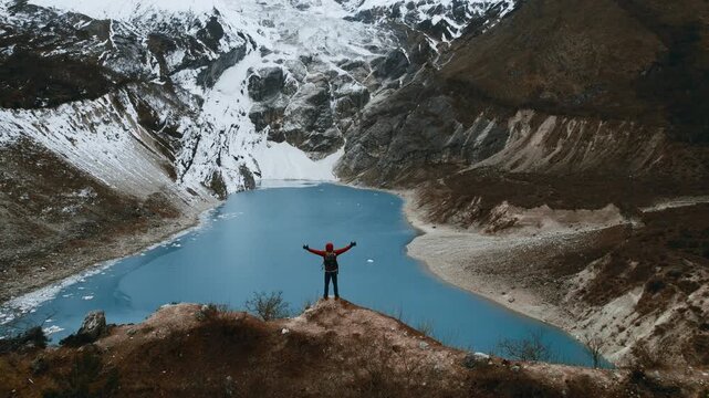 Cinematic footage of a solo adventurer celebrating at the breathtaking Birendra Lake viewpoint, with arms outstretched against a backdrop of vivid blue water and majestic Himalayan glaciers.