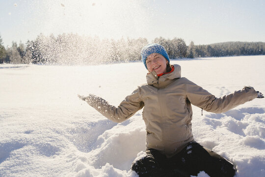 Smiling woman playing with snow while sitting on land at sunny day