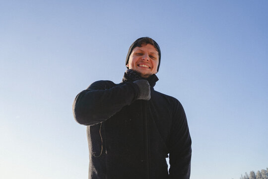 Low angle portrait of smiling man closing zipper white standing against clear sky