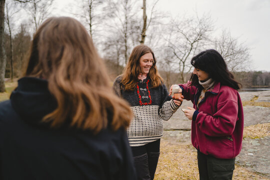 Woman giving milk to female friend in bottle cap while standing at outdoor location