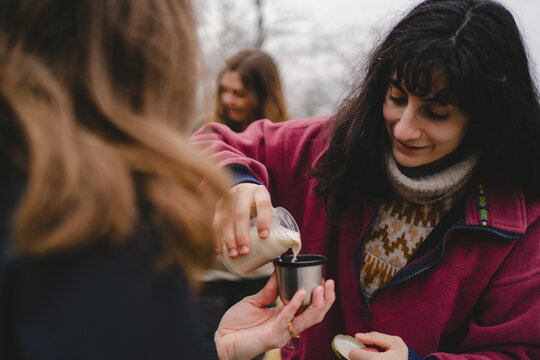Woman pouring milk in bottle cap held by female friend