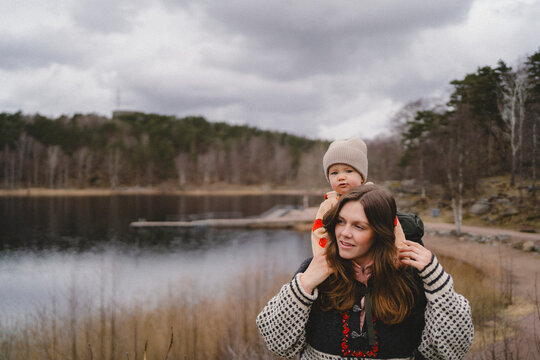 Mother piggybacking toddler son while walking near lake