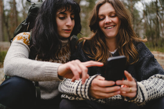 Female friends surfing on smart phone while spending leisure time in forest
