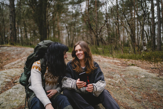 Happy woman talking with female friend sitting on rock in forest