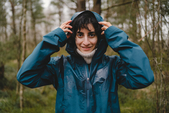 Portrait of smiling woman wearing raincoat standing in rain at forest