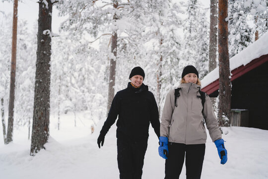 Smiling couple dressed in warm clothes walking on snow in winter forest