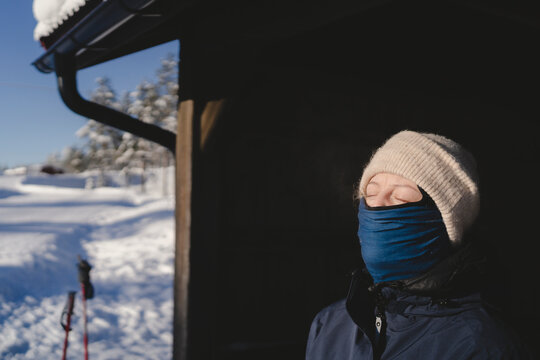 Woman with eyes closed covering face with balaclava and knit hat in winter season