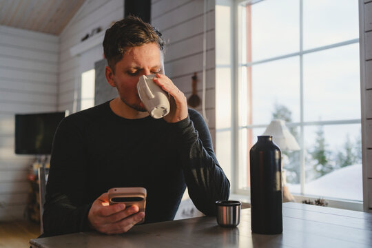 Man holding phone and sipping coffee while sitting in cabin