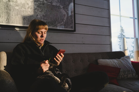 Woman scrolling smart phone while sitting on sofa in cabin