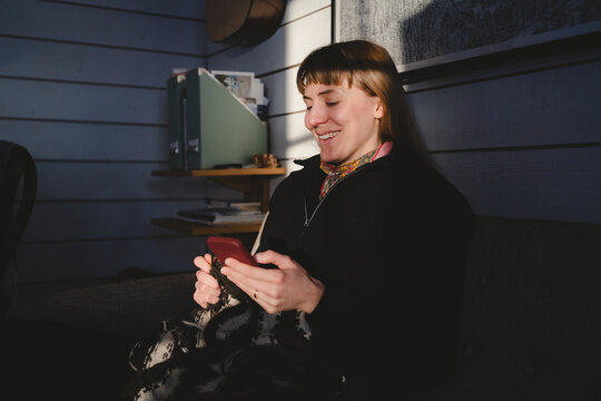 Smiling woman using smart phone sitting on sofa in cabin