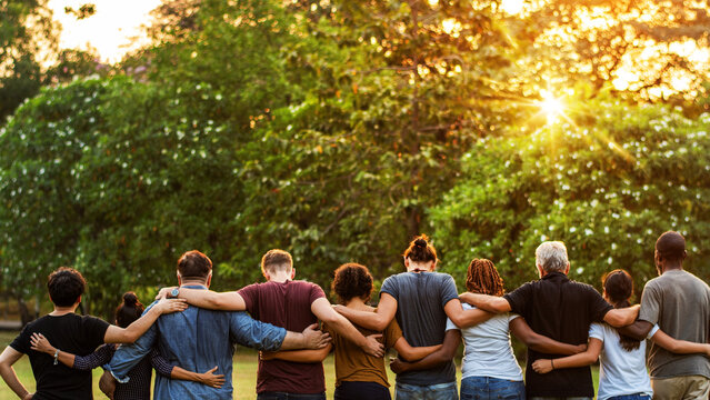 Diverse group of people standing outdoors, arms around each other.
