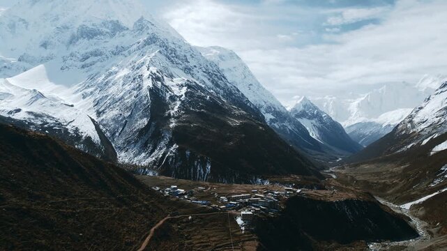 A wide view of a vast Himalayan valley with the snow-capped Manaslu massif towering above a small village in Nepal.