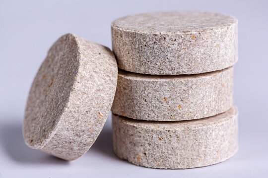 A stack of round, beige, textured tablets or pills on a plain background