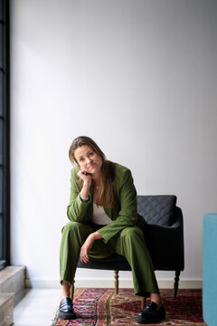 Portrait of female business entrepreneur leaning on elbow while sitting at armchair in office