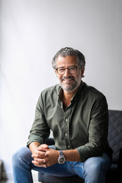 Portrait of smiling male business professional sitting with hands clasped in new office