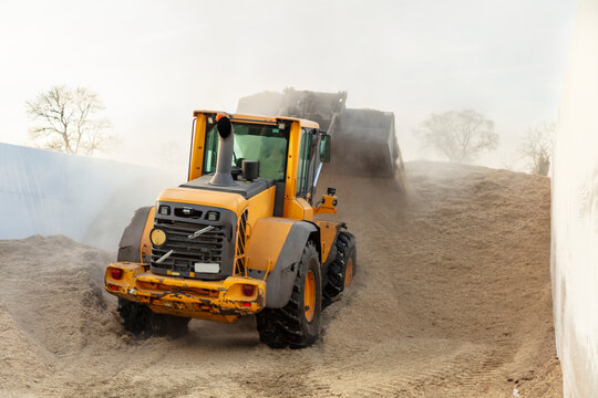 Backhoe making heap of massive silage at farm