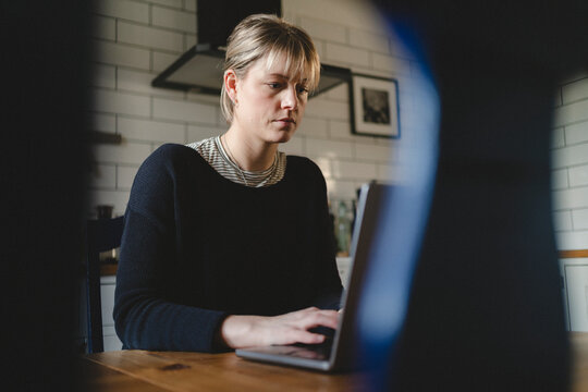 Concentrated blond businesswoman working on laptop while sitting at table in home