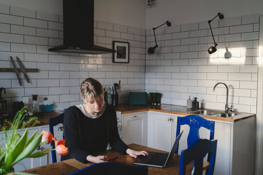 Woman using wireless technologies while sitting at table in home