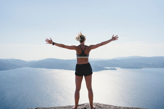 Rear view of woman standing with arm outstretched on hill against sea at sunny day