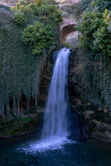 Obraz premium Scenic waterfall with metal water gate flowing between traditional stone houses in a rural village