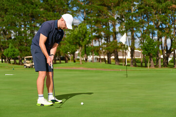 Obraz premium Man putting golf ball on green course.