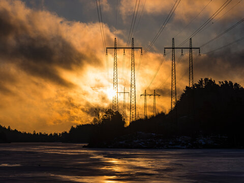 Scenic view of electricity pylons near sea against cloudy sky at sunset