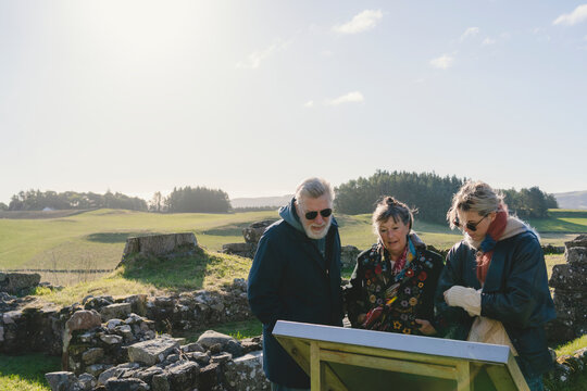 Woman with parents reading interpretive panel while standing at remote location against sunny sky