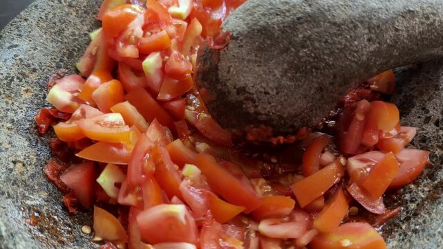 Crushing Fresh Tomatoes and Chili in Traditional Stone Mortar and Pestle for Indonesian Sambal