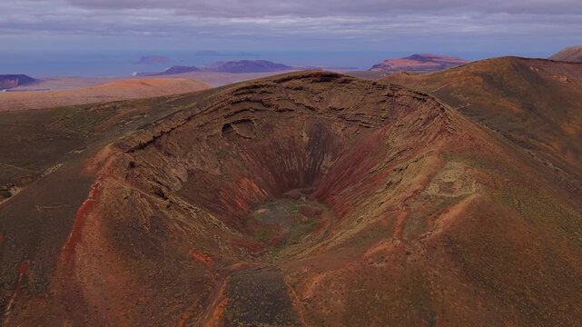 Colorful crater of dormant volcano in Lanzarote, with La Graciosa island visible on horizon, Spain. Aerial backward
