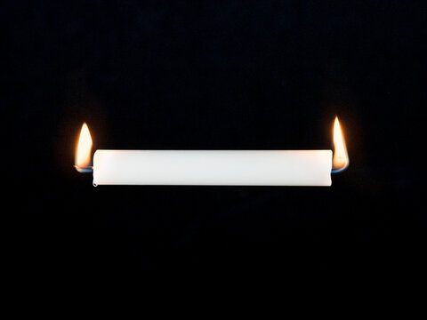 White candle burning at both ends against black background