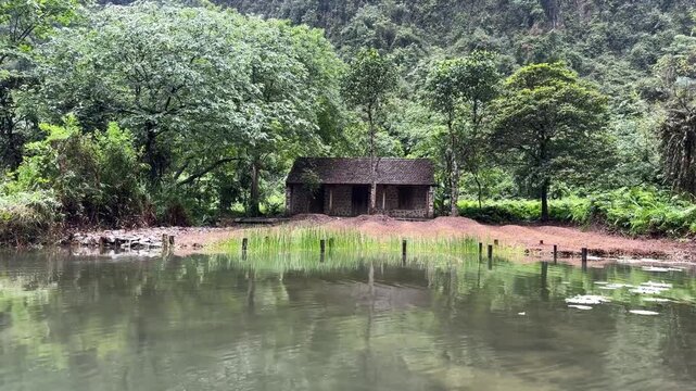 Small stone hut by the river in Ninh Binh, lush tropical greenery, rural landscape, quiet retreat, nature travel scenery