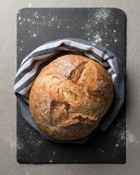 Directly above shot of freshly baked sourdough loaf wrapped in striped linen napkin on slate board