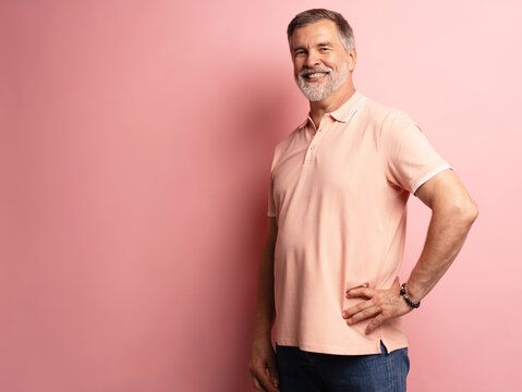 Portrait of smiling happy mature grey-haired man standing on pink background